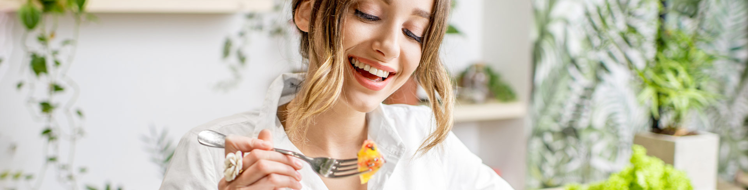 Nasmejana žena jede zdravu salatu za stolom