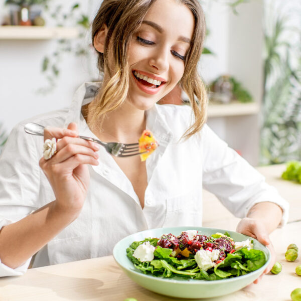 Nasmejana žena jede zdravu salatu za stolom