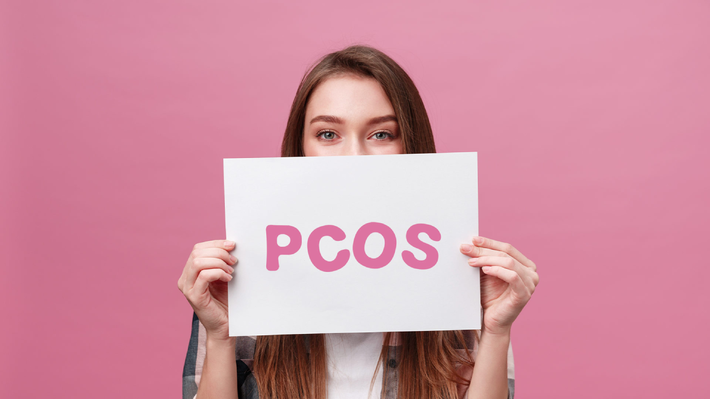 Žena drži znak PCOS na ružičastoj pozadini