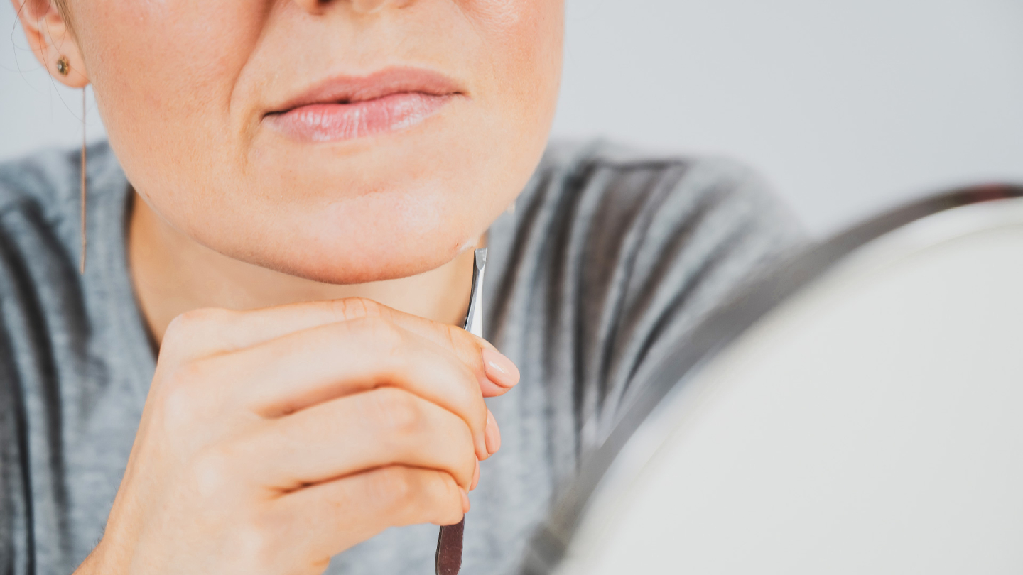 Žena uklanja dlačice sa brade pincetom, krupni plan